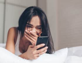 Woman lying on bed laughing at something on her phone.