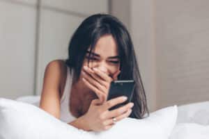 Woman lying on bed laughing at something on her phone.