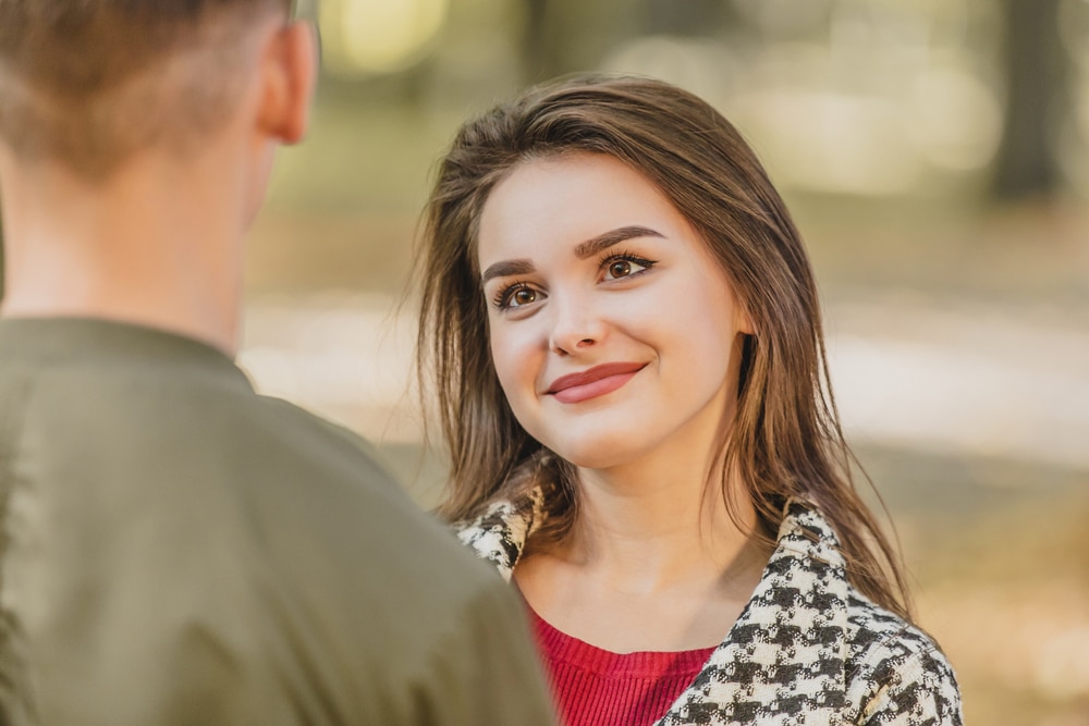 A smiling young woman looking at a man who is facing away from the camera.