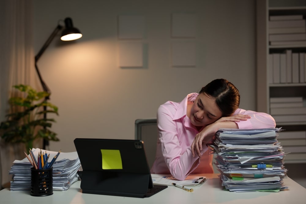 Women sleeping at her desk on a stack of papers.